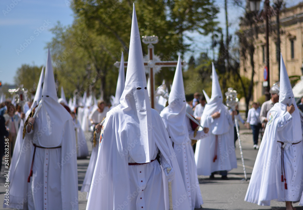 a large Catholic procession with penitents dressed in white and with a hood
