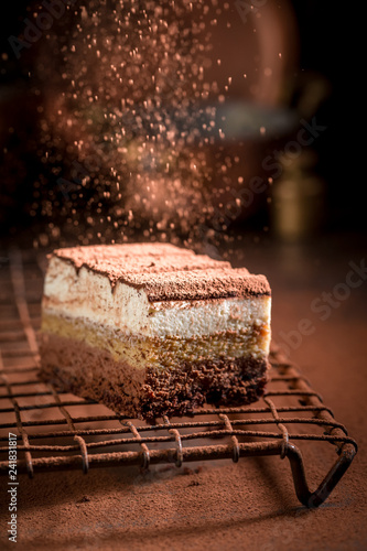 Photos Falling cocoa powder on tiramisu cake on metal cooling grid