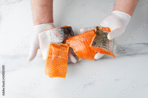 Chef proposing several pieces of salmon.White kitchen marble table,male hands, raw salmon