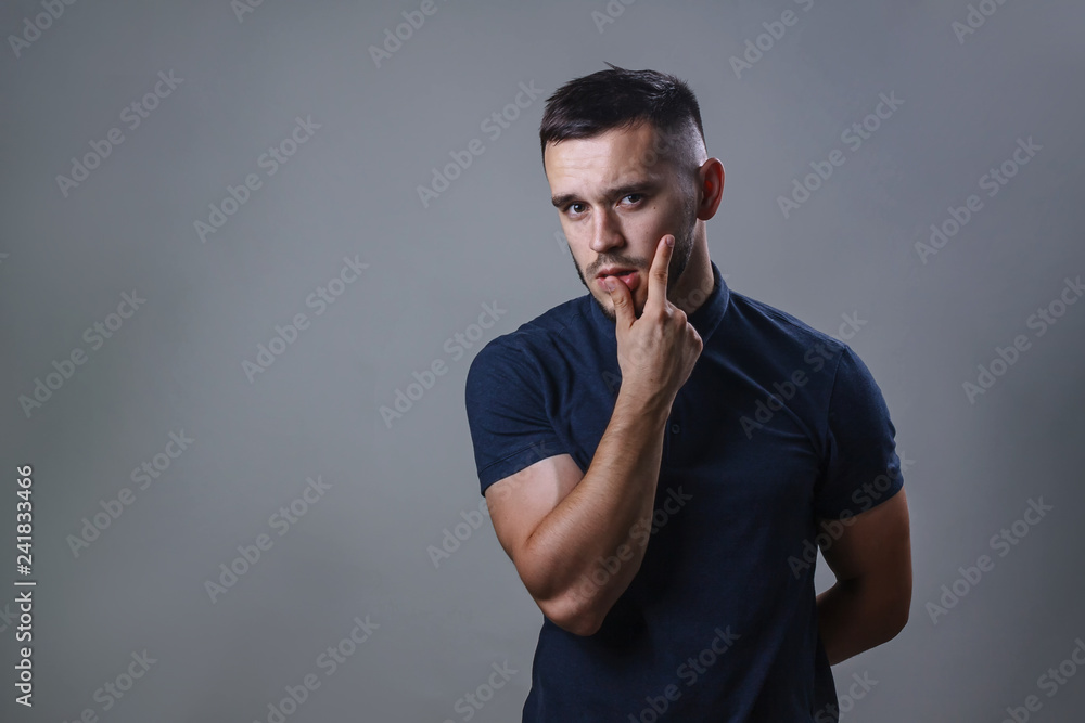 Portrait of a thoughtful look man. Handsome young man thinking on something his hand is near the mouth, isolated on gray background Portrait of a thoughtful look man. Handsome young man thinking on something his hand is near the mouth, isolated on gray background