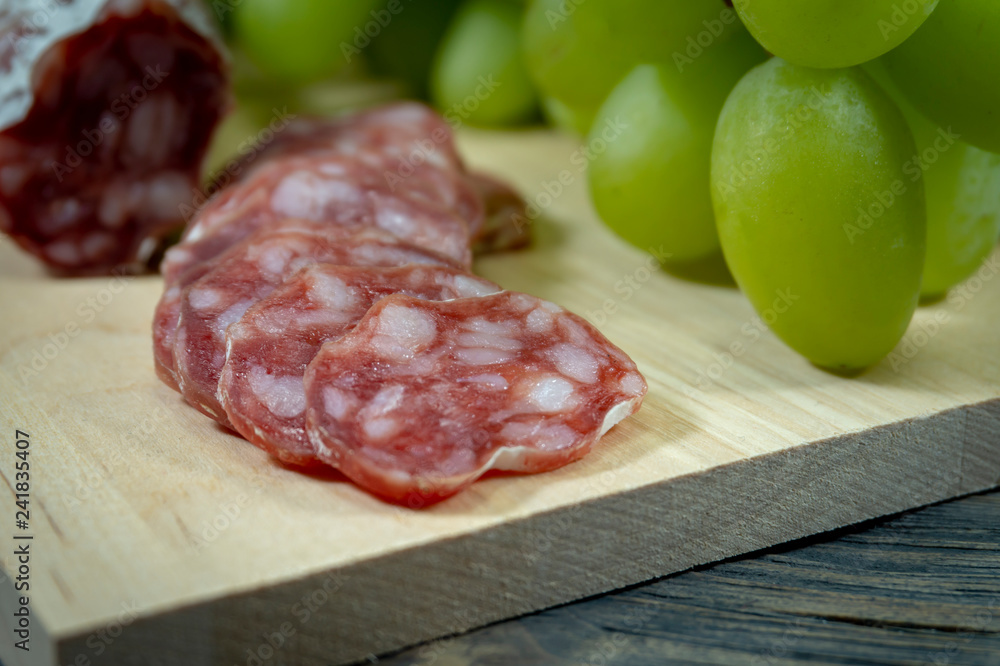 Sliced salami and grapes on wooden cutting board Sliced salami and grapes on wooden cutting board