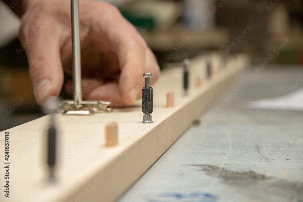 The furniture maker assembles the Cabinet, he tightens the screws with a screwdriver . The furniture maker assembles the Cabinet, he tightens the screws with a screwdriver .