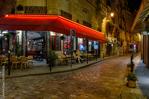 Cozy street with tables of cafe in Paris at night, France