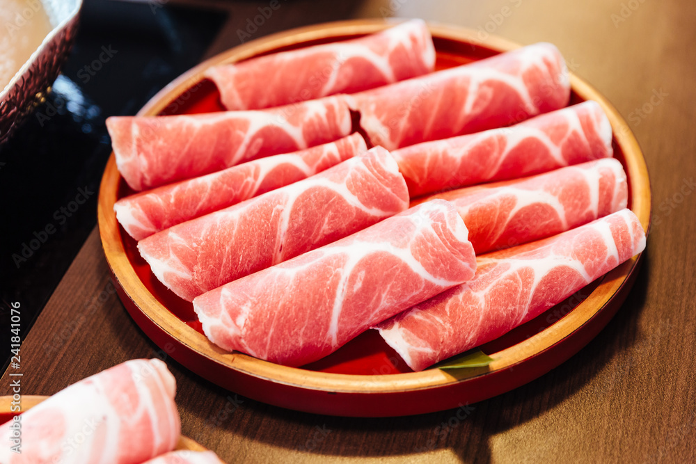 Premium Rare Slices Kurobuta (Black Pig) pork with high-marbled texture on circle wooden plate served for Sukiyaki and Shabu.