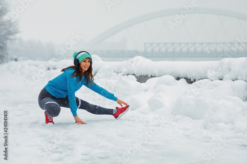 Young woman stretching legs on snowy day in the city