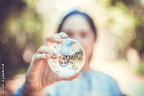 Beautiful woman hold crystal ball and can see a nice view that reflects through the big marble ball. Filtered image.