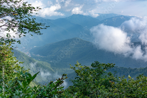 The view from the height of the valley, surrounded by high green mountains through trees, clouds and fog. Caucasus, Russia