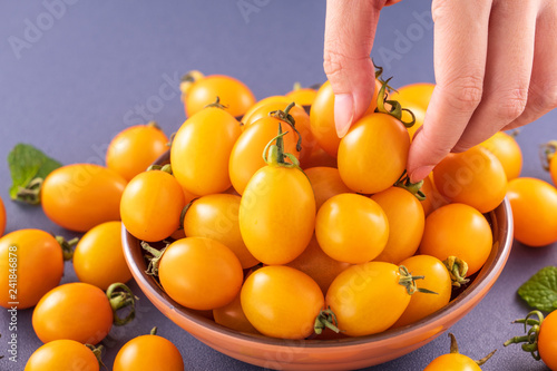 Fresh cherry tomatoes in a wooden bowl with a young woman is picking them with hand isolated on a blue background, close up, copy space photo