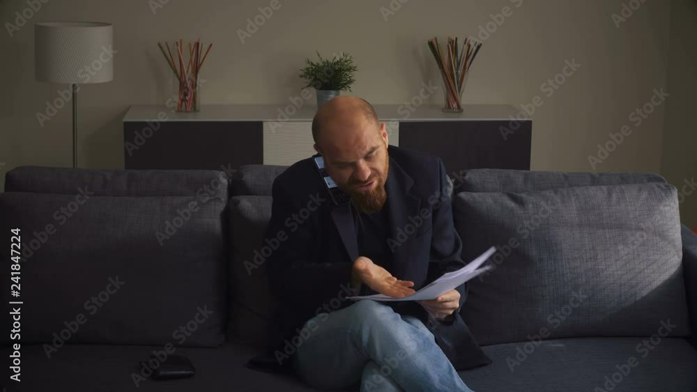 Angry Businessman With Documents Talking On Cellphone Sitting On couch. Angry Businessman With Documents Talking On Cellphone Sitting On couch.