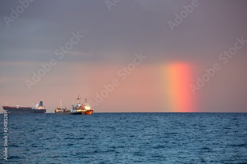 Seascape with amazing rainbaw half covered with heavy rainy clouds in sky  intensively colored  three ships on horiozn