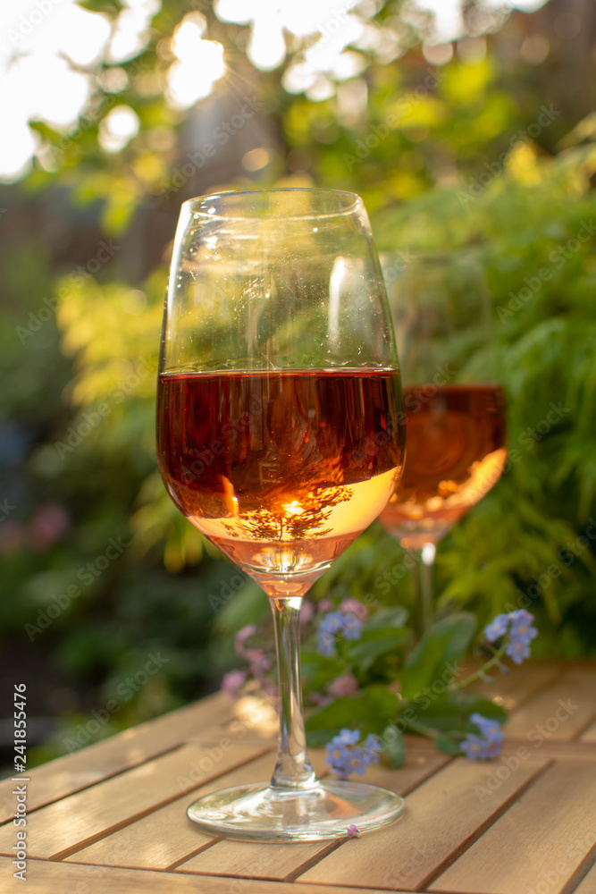 Two cold rose wine glasses served on outdoor terrace in garden with flowers in sunny day Two cold rose wine glasses served on outdoor terrace in garden with flowers in sunny day