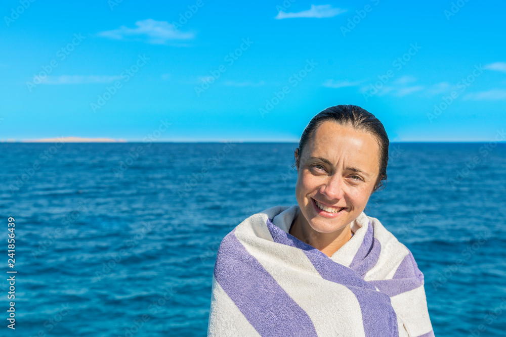 beautiful woman in a towel by the sea. Portrait of preteen brunette woman, wet and wrapped in towel after swimming, against blue sea and sky.