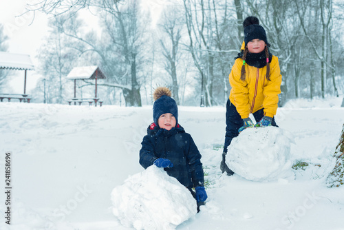portrait of brother and sister. little boy and girl make snowman in winter.