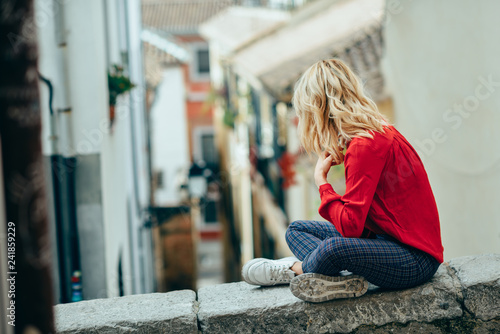 Young blonde tourist woman sitting outdoors looking a beautiful narrow street