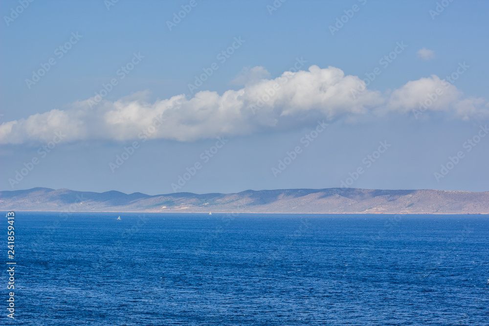 vivid sea blue water scenic landscape and opposite coast line in fog on blue sky background with cloud, picturesque wallpaper pattern for poster or banner