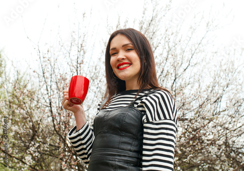 Portrait of a beautiful woman in sripped sweater with cup in blossom apple tree garden in spring time photo