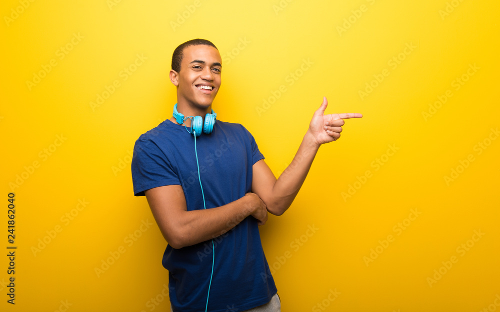 African american man with blue t-shirt on yellow background pointing finger to the side in lateral position African american man with blue t-shirt on yellow background pointing finger to the side in lateral position