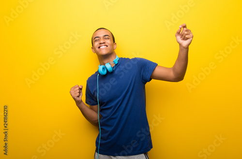 African american man with blue t-shirt on yellow background enjoy dancing while listening to music at a party © luismolinero