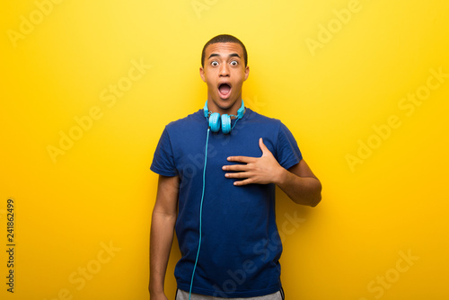 African american man with blue t-shirt on yellow background surprised and shocked while looking right © luismolinero