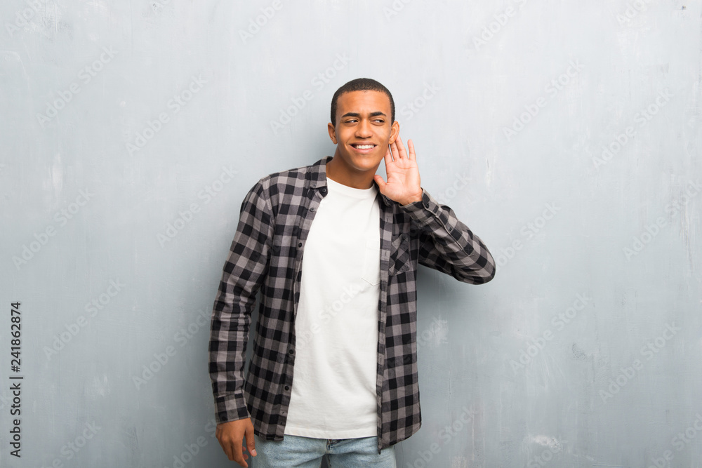 Young african american man with checkered shirt listening to something by putting hand on the ear