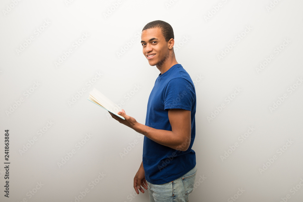 Young african american man on white wall holding a book and enjoying reading Young african american man on white wall holding a book and enjoying reading