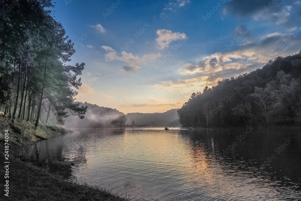 sunrise at Pang Oung, beautiful lake view misty morning of soft mist moving on the water with reflection of pine forest on water and colorful of sun light in the sky background, Mae Hong Son, Thailand