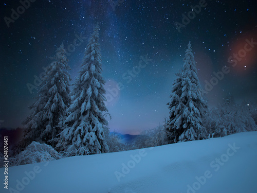 Fairy-tale starry night in the Ukrainian Carpathian mountains with the galaxy Milky way in the sky and the glow of the full moon Winter frosty time on the background of a cozy little house. © kishivan