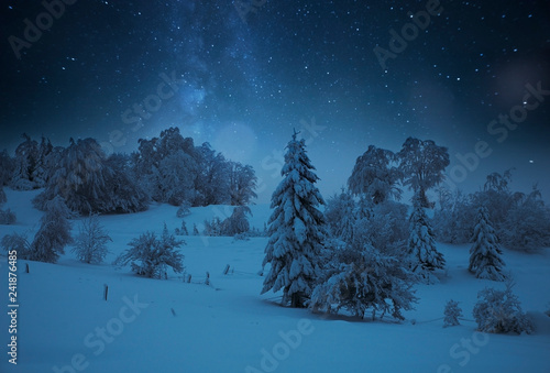 Fairy-tale starry night in the Ukrainian Carpathian mountains with the galaxy Milky way in the sky and the glow of the full moon Winter frosty time on the background of a cozy little house.