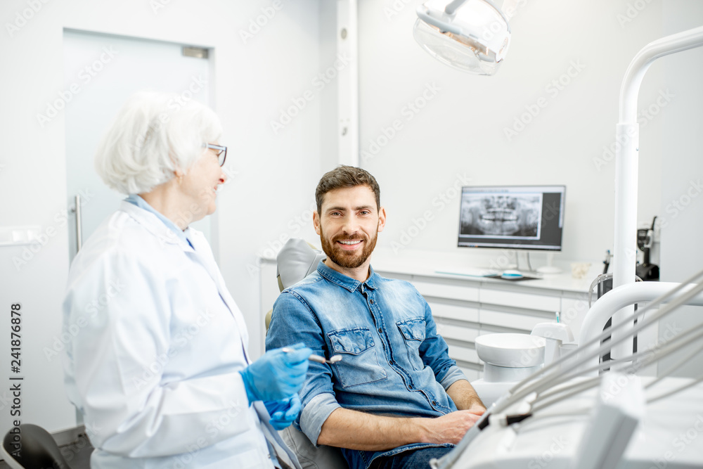 Obraz premium Portrait of a handsome male patient in blue shirt with elderly woman dentist in the dental office