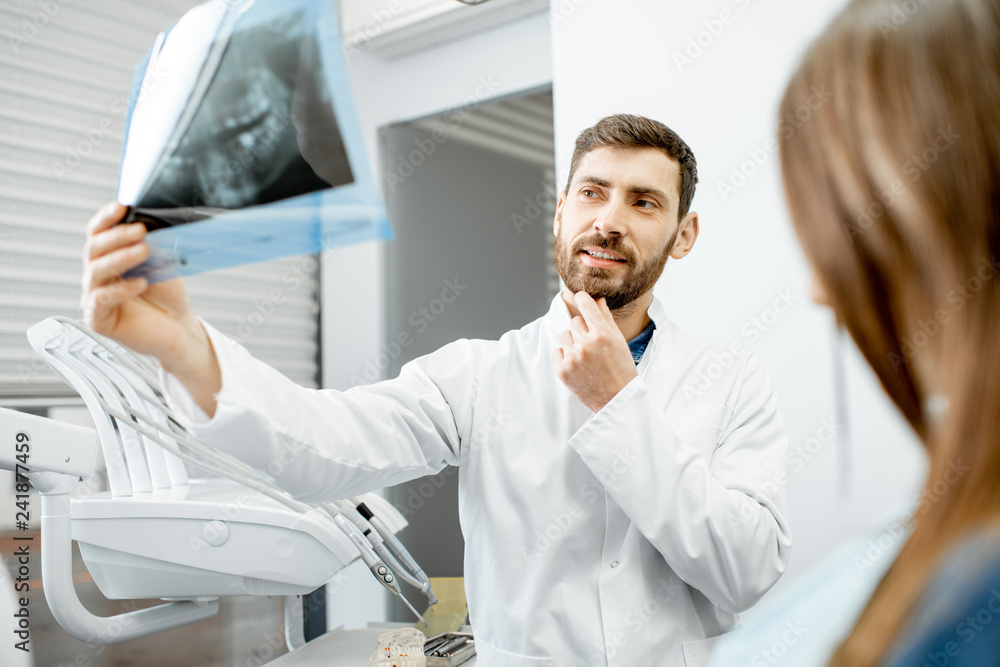 Handsome dentist checking panoramic x-ray of a jaw during the medical consultation with woman patient in the dental office Handsome dentist checking panoramic x-ray of a jaw during the medical consultation with woman patient in the dental office