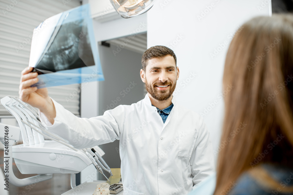 Handsome dentist checking panoramic x-ray of a jaw during the medical consultation with woman patient in the dental office Handsome dentist checking panoramic x-ray of a jaw during the medical consultation with woman patient in the dental office