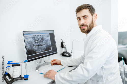 Portrait of a dentist in medical gown working with computer in the dental office