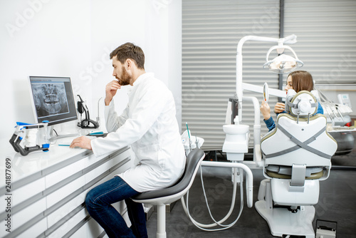 Dentist working with computer in the dental office with woman patient on the background