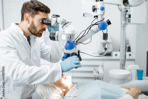 Male dentist examining senior woman looking on the teeth with professional microscope in the surgery dental office