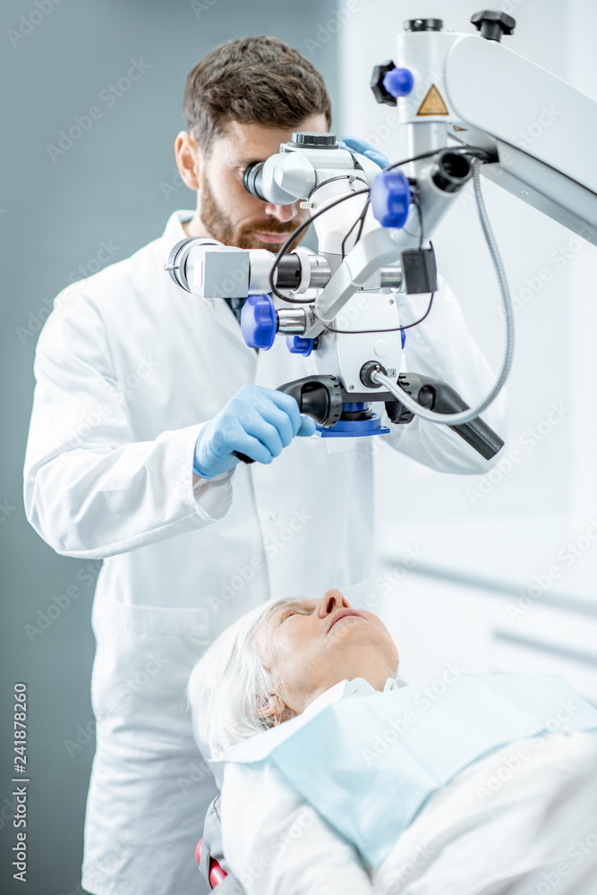 Male dentist examining senior woman looking on the teeth with professional microscope in the surgery dental office Male dentist examining senior woman looking on the teeth with professional microscope in the surgery dental office