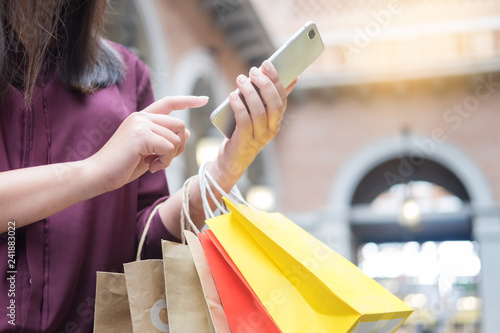 Woman look at mobile phone with paperbags in the mall while enjoying a day shopping.