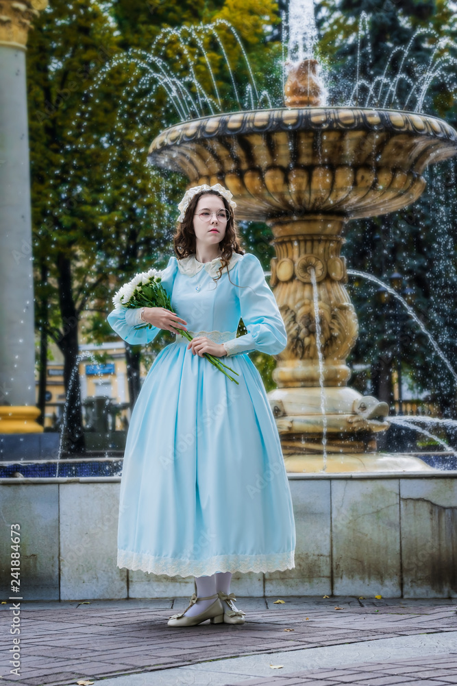 Girl with a bouquet in vintage dress standing by fountain