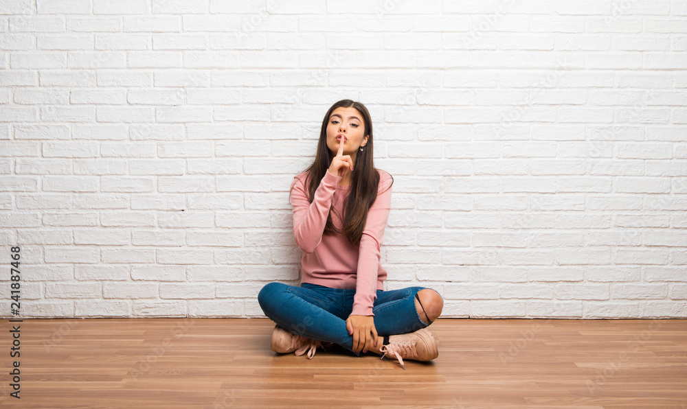 Teenager girl sitting on the floor in a room showing a sign of silence gesture putting finger in mouth Teenager girl sitting on the floor in a room showing a sign of silence gesture putting finger in mouth