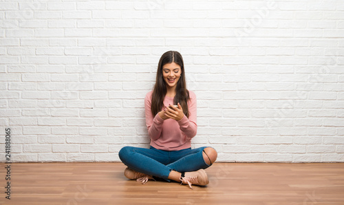 Teenager girl sitting on the floor in a room sending a message with the mobile