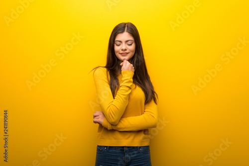 Teenager girl on vibrant yellow background looking down with the hand on the chin
