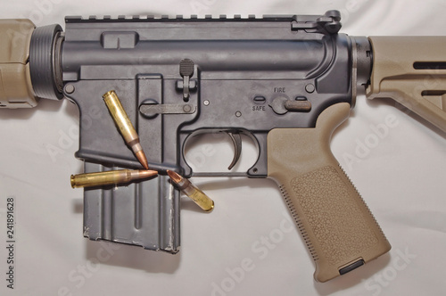 The upper of a black and brown 223 caliber AR-15 rifle with a magazine inserted and three 223 caliber rifle bullets with it on a white background photo