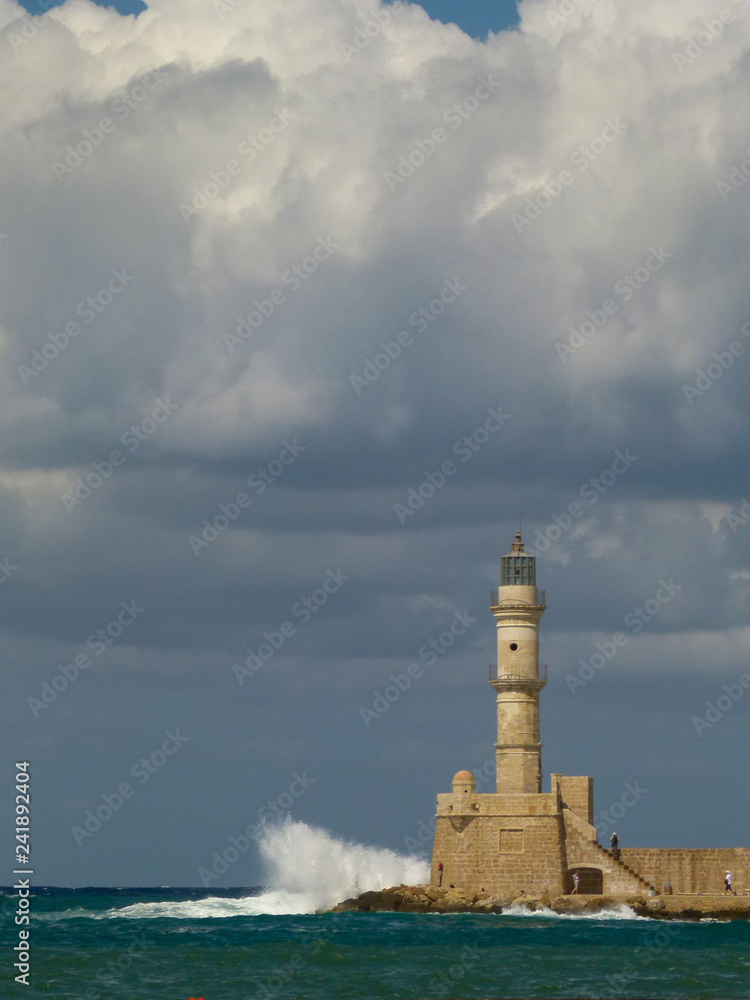 White waves with a lot of spray are beating on the lighthouse in Chania under a gloomy sky