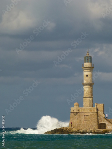 White waves with a lot of splashes crash into Chania lighthouse under a gray sky with clouds