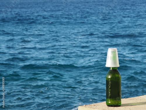 Wallpaper Mural a bottle of beer with a plastic cup on top. blue sea background. sunny day. Torontodigital.ca