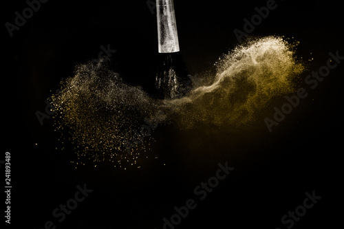 Cosmetic brush with golden cosmetic powder spreading for makeup artist in black background, look like a luxury mood.