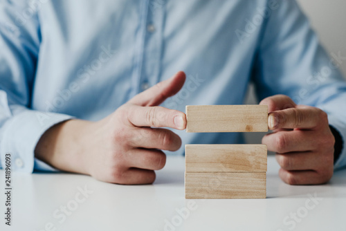 Businessman in a blue shirt arranges wooden jigsaw blocks. The man arranges empty blocks one on top of the other. Different concepts to supplement with content. Business concept, HR.