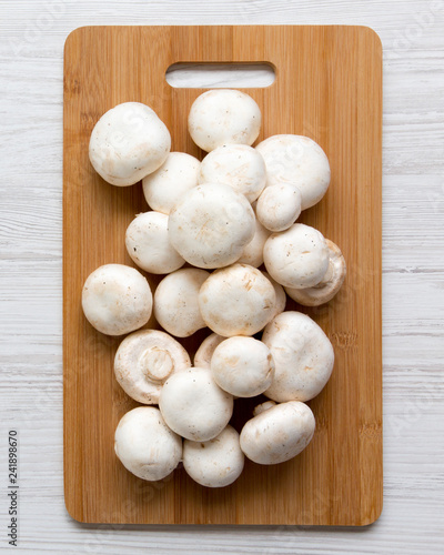 Champignon mushrooms on bamboo board on a white wooden background, top view. From above. Close-up.