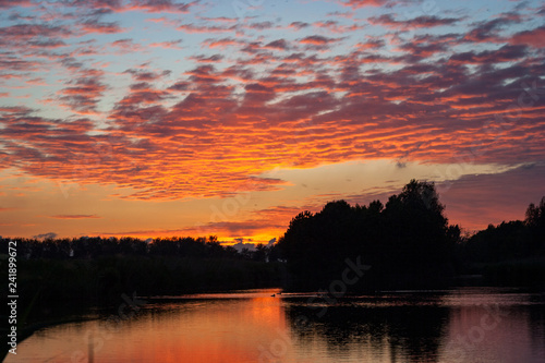 Altocumulus clouds over a lake are beautifully colored by the orange and purple light of the setting sun. Tranquil scene on an evening in spring, close to the city of Gouda, Holland.