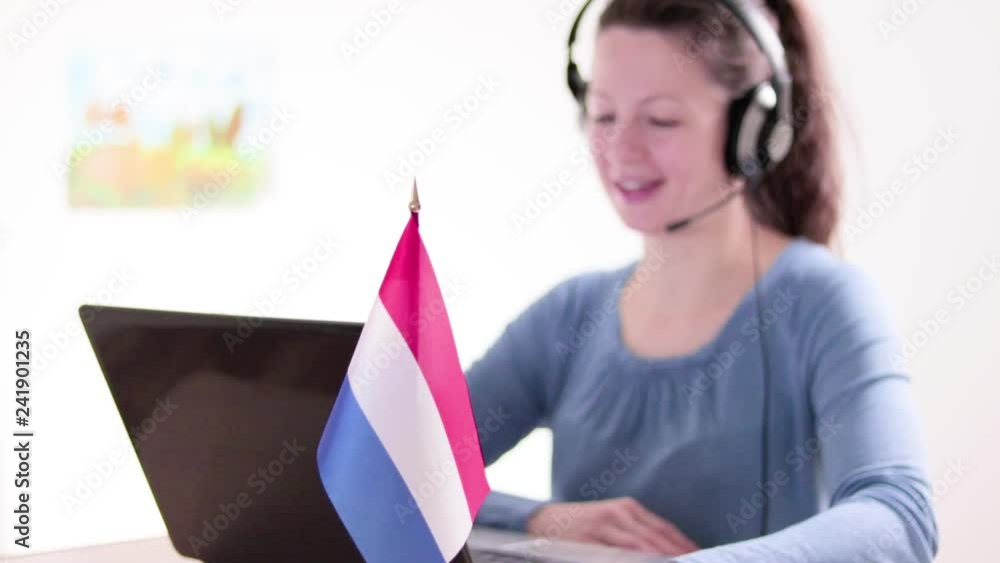 Young beautiful smiling woman sitting in front of a laptop with a French flag on the table and communicating on a computer using a headset Young beautiful smiling woman sitting in front of a laptop with a French flag on the table and communicating on a computer using a headset