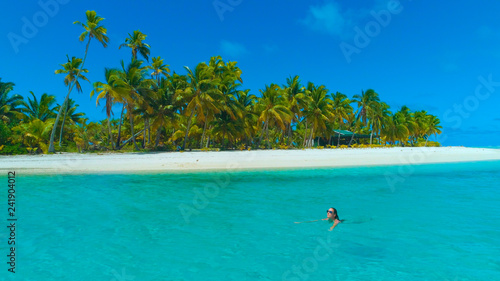 DRONE: Happy female traveler swimming along the picturesque white sand beach.